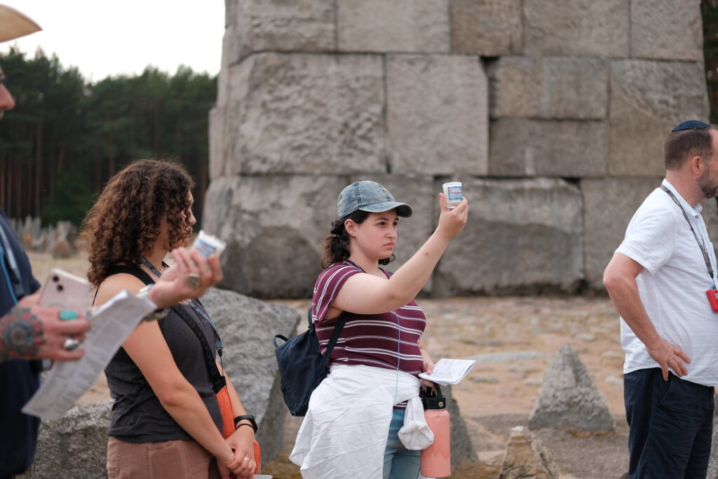 young woman holds up candle at remains of concentration camp