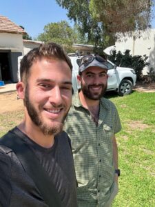 Two men stand in front of a white truck