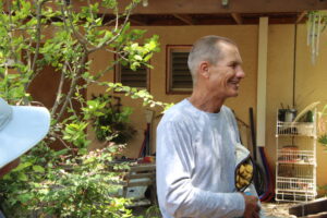 Nitzan, a middle-aged man in his 60s stands in front of a house, smiling. 